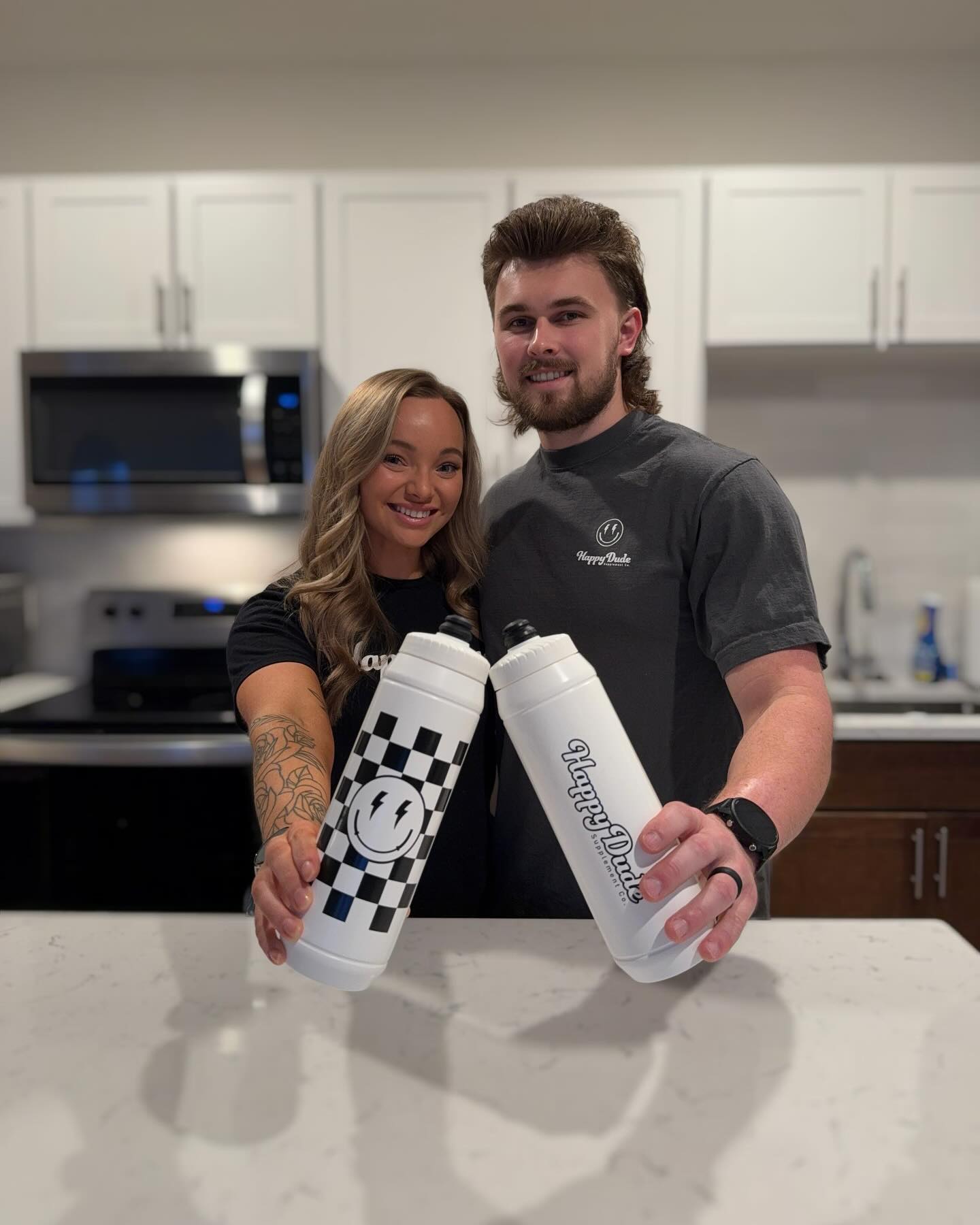 Two people holding happy dude supps white water bottles with logos in a kitchen.